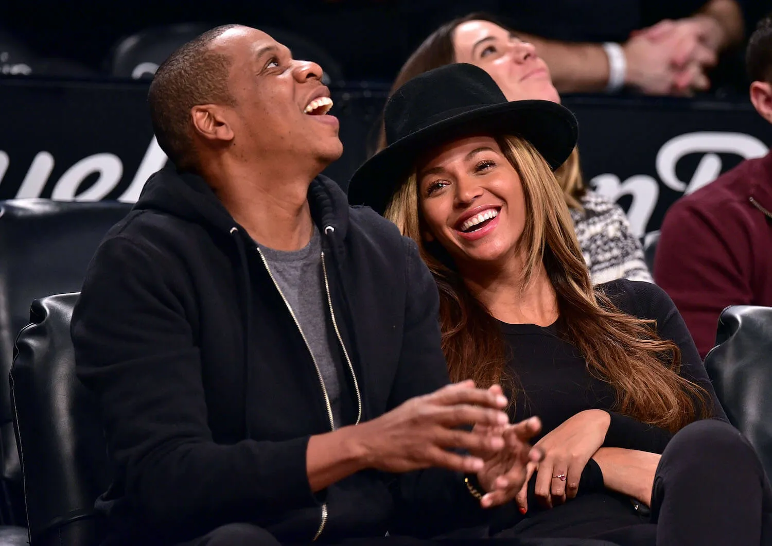 Jay-Z looking up and laughing next to Beyoncé at an NBA game