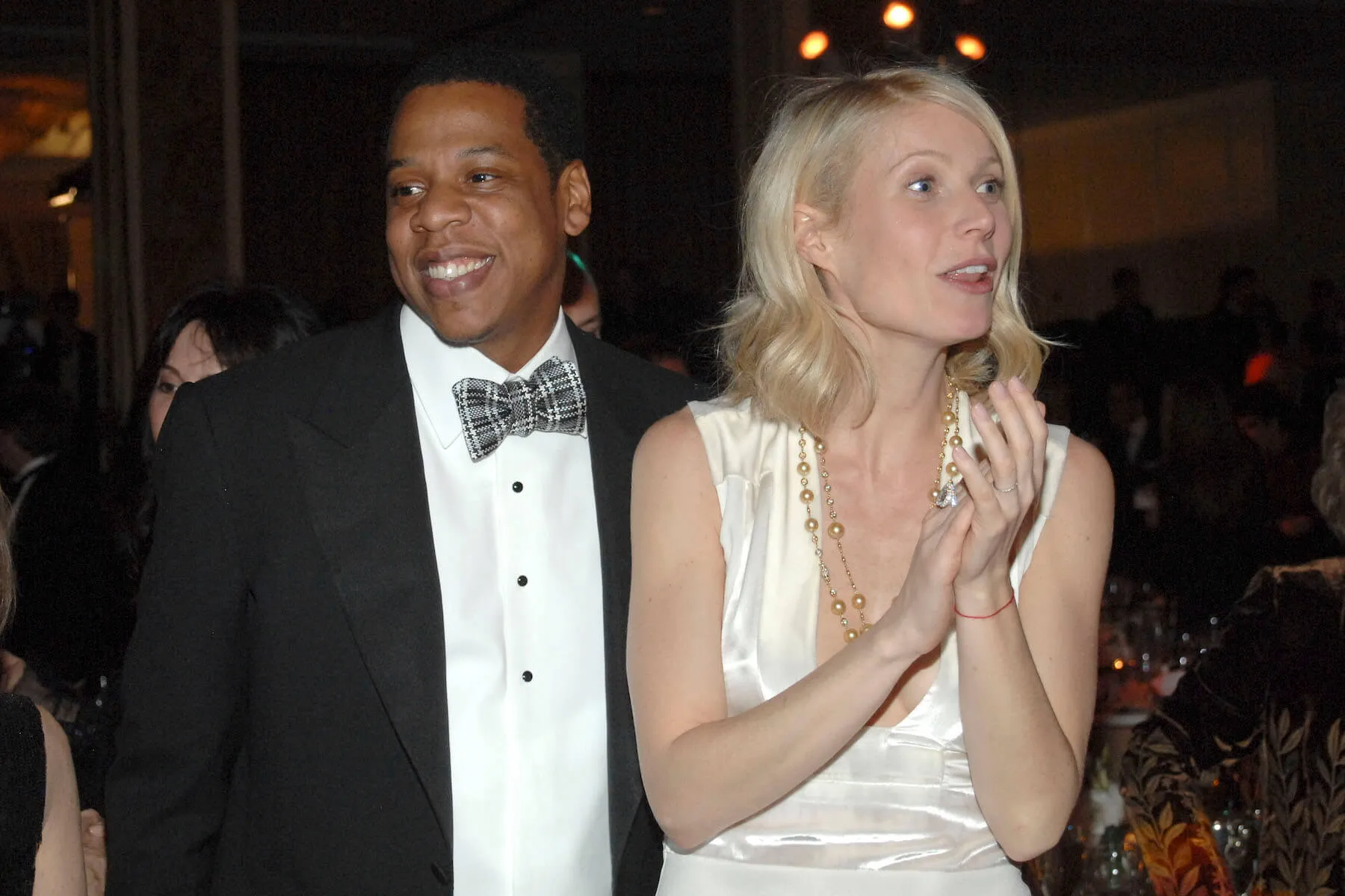 Jay-Z smiling in a suit while standing next to Gwyneth Paltrow, who's in a white dress and clasping her hands together, in 2009