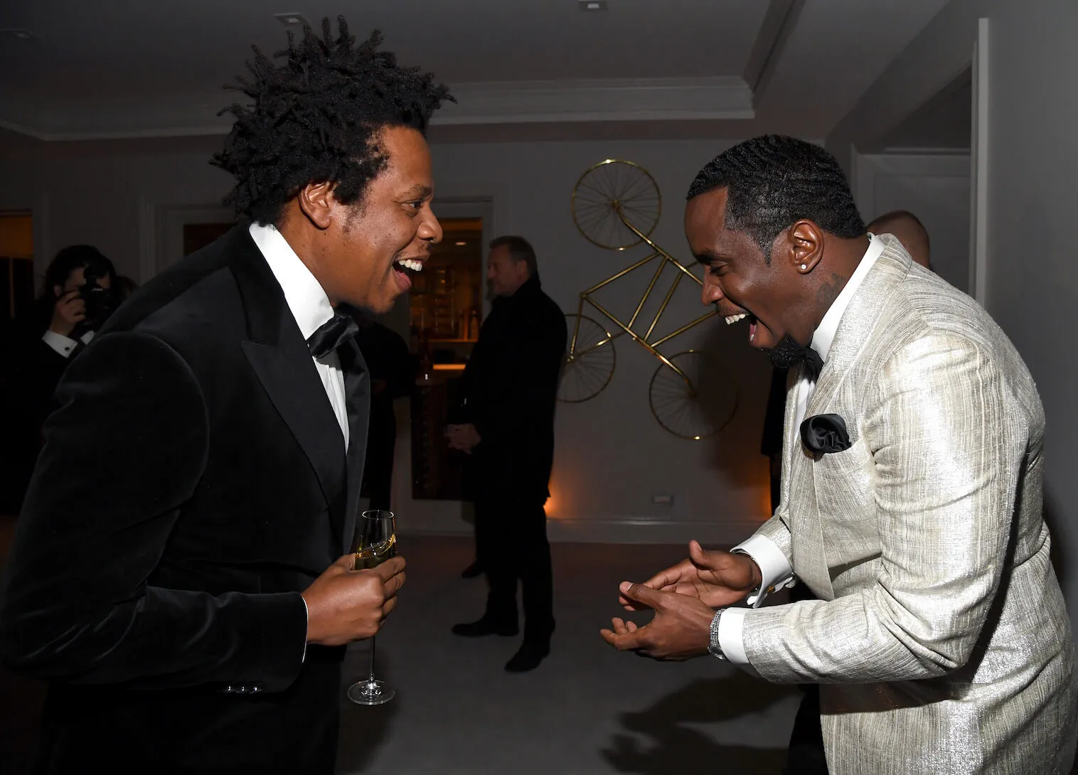 Jay-Z and Sean 'Diddy' Combs in suits facing each other and laughing at a party