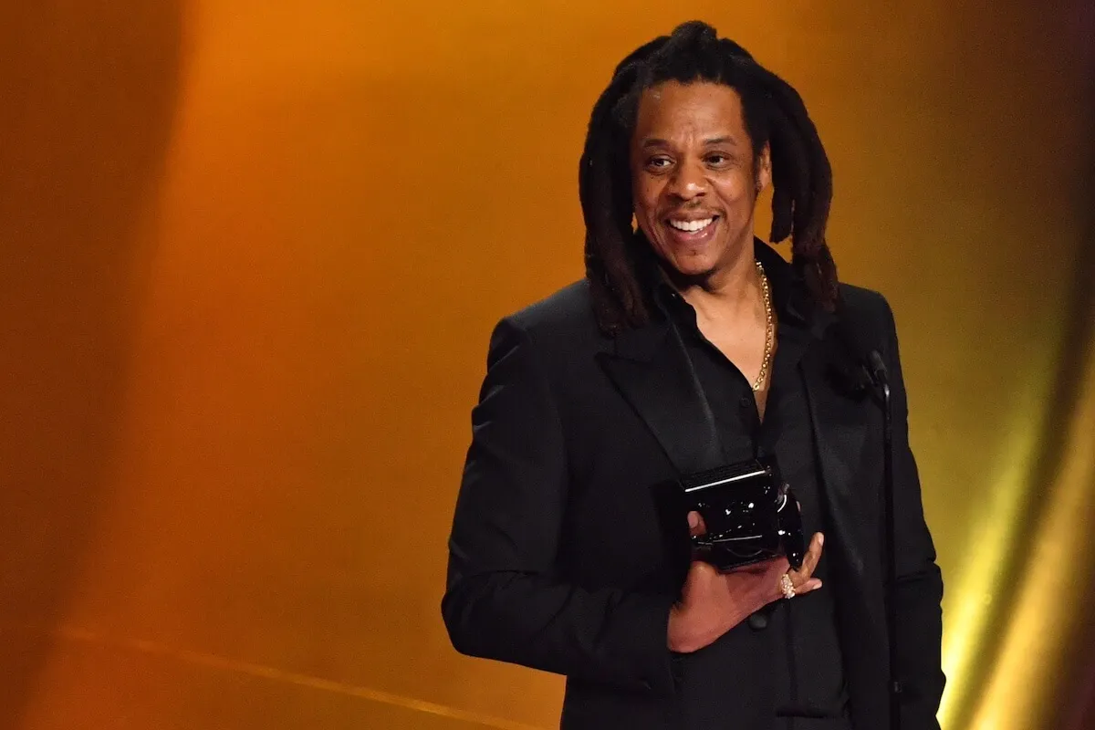 Jay-Z wears a black suit and holds an award.