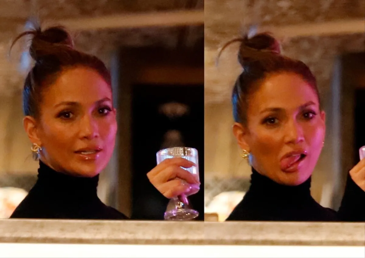 Wearing a black turtleneck, Jennifer Lopez sticks her tongue out at the paparazzi while holding a drink