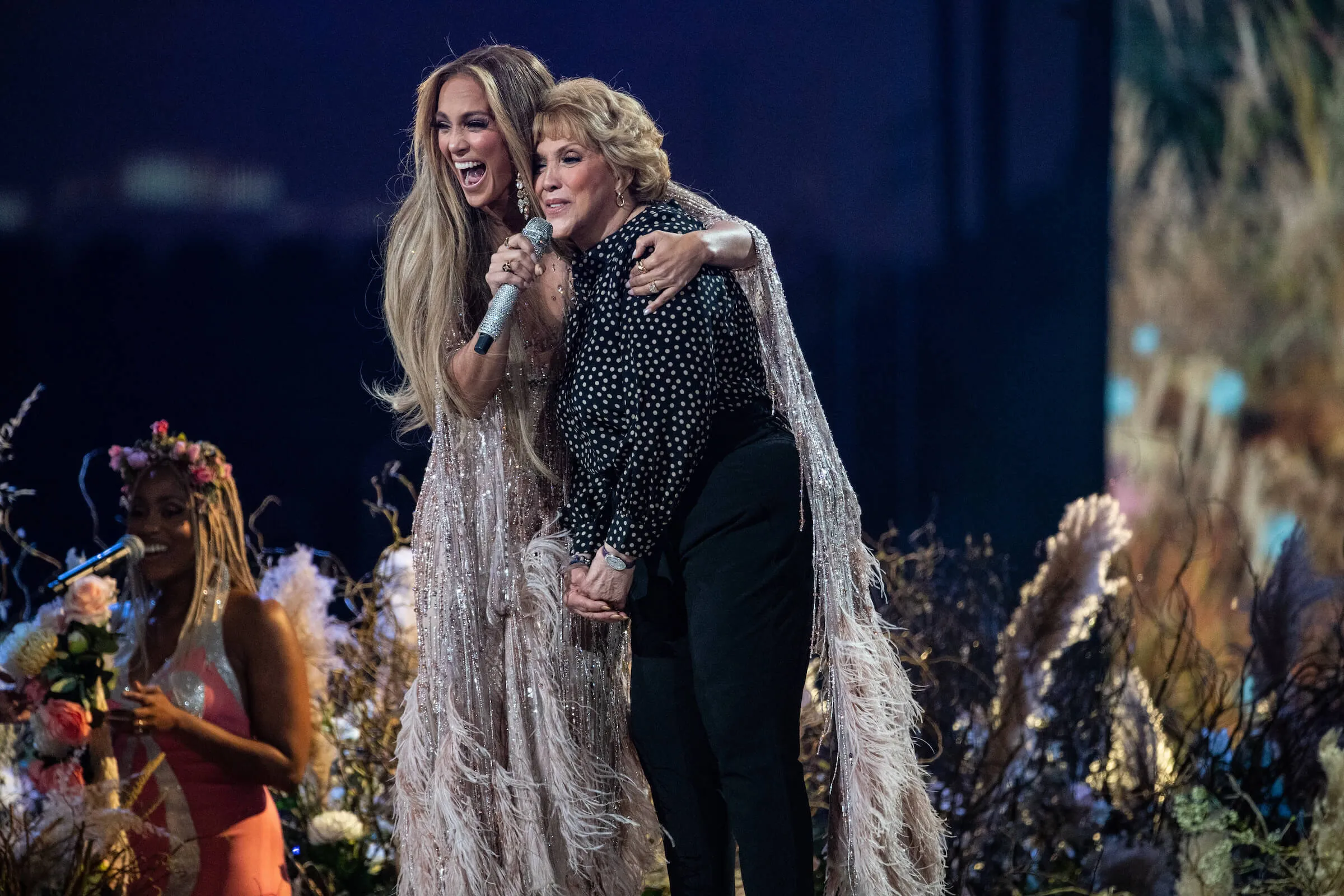 Jennifer Lopez on stage with her mother, Guadalupe Rodríguez. Lopez is smiling and holding a microphone up to her mom.