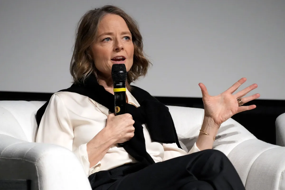 Jodie Foster wearing a white shirt and holding a microphone at an event in 2024