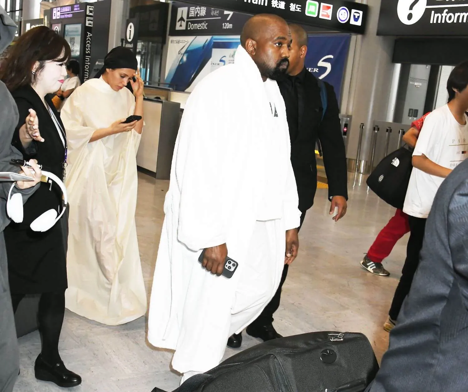 Kanye West and Bianca Censori walking through the airport in Japan in June 2024. Censori is looking down at her phone behind West.