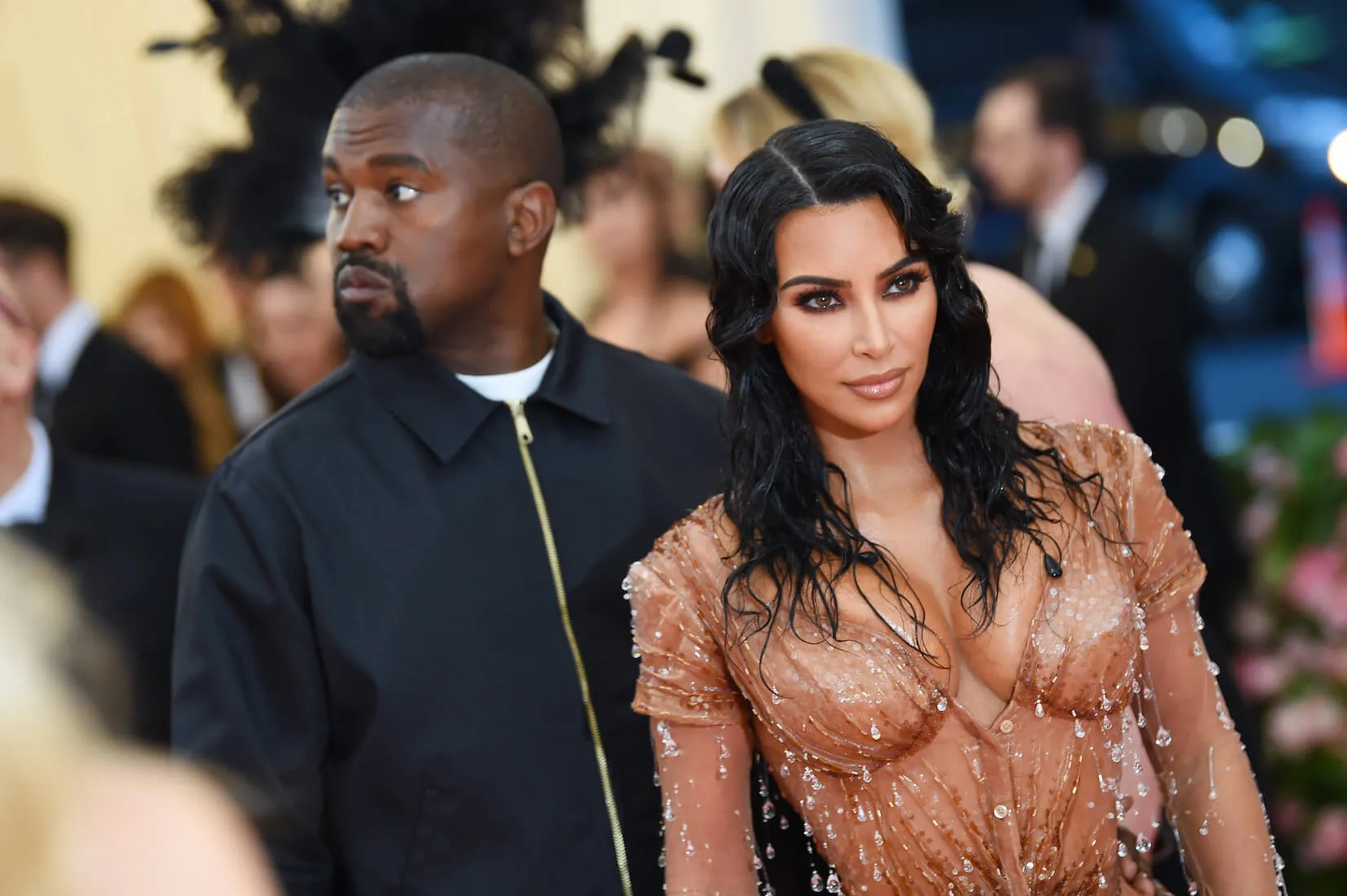 Kanye West and Kim Kardashian posing at the Met Gala in 2019. Kardashian is looking forward and wearing a gold dress while West looks over his right shoulder and stands behind her.