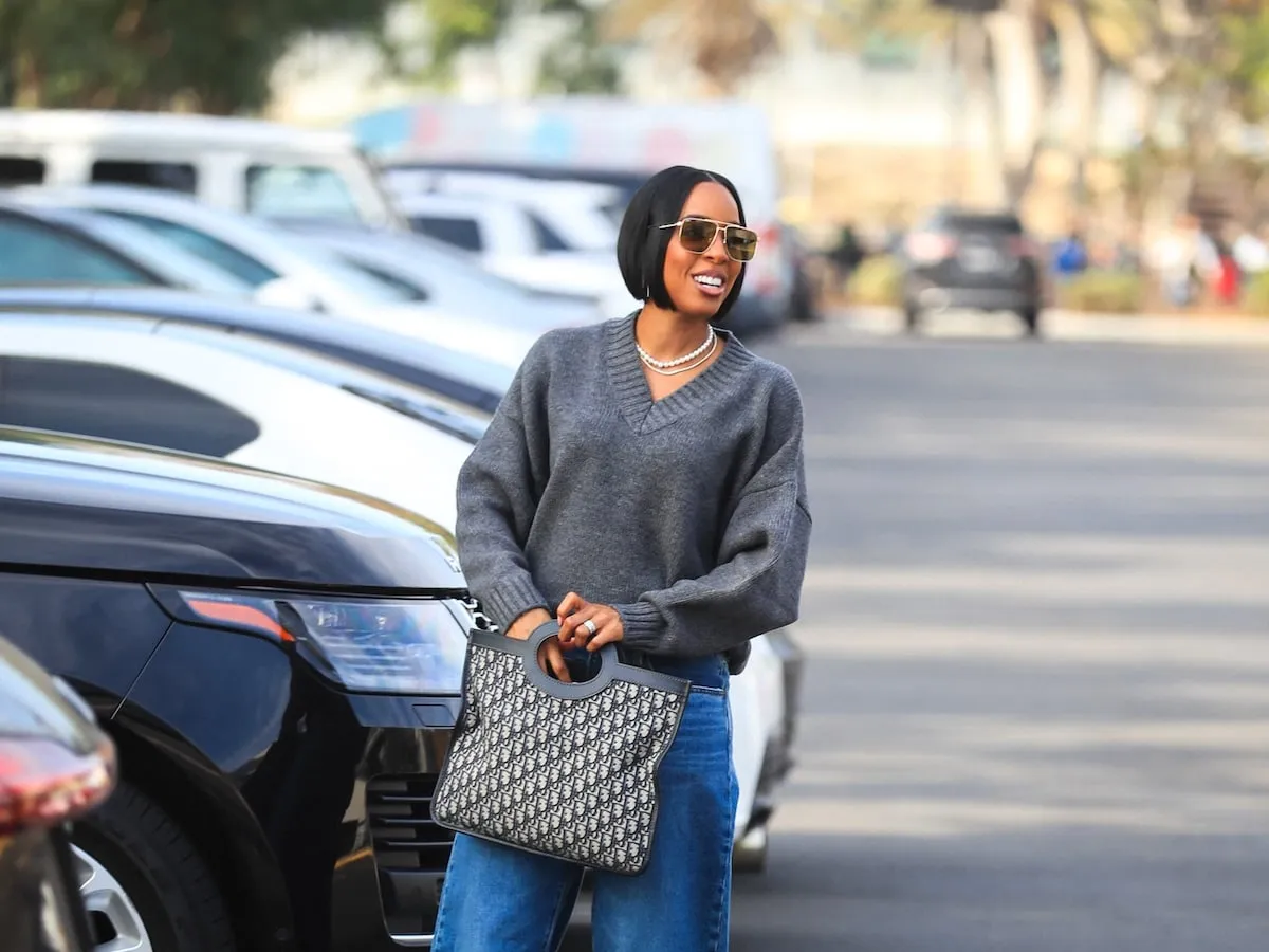 Wearing a gray sweater and baggy jeans, Kelly Rowland walks through the parking lot at LA's BMO Stadium