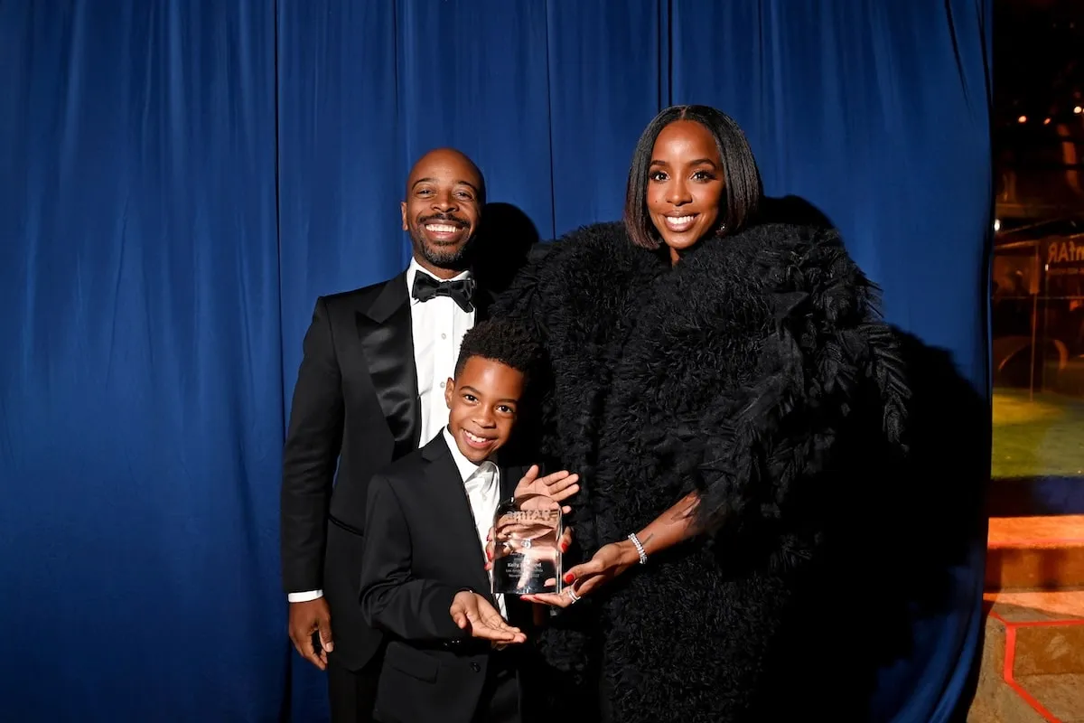 Wearing black tie outfits, Tim Weatherspoon, Titan Jewell Weatherspoon, and Kelly Rowland smile together at the amfAR Gala