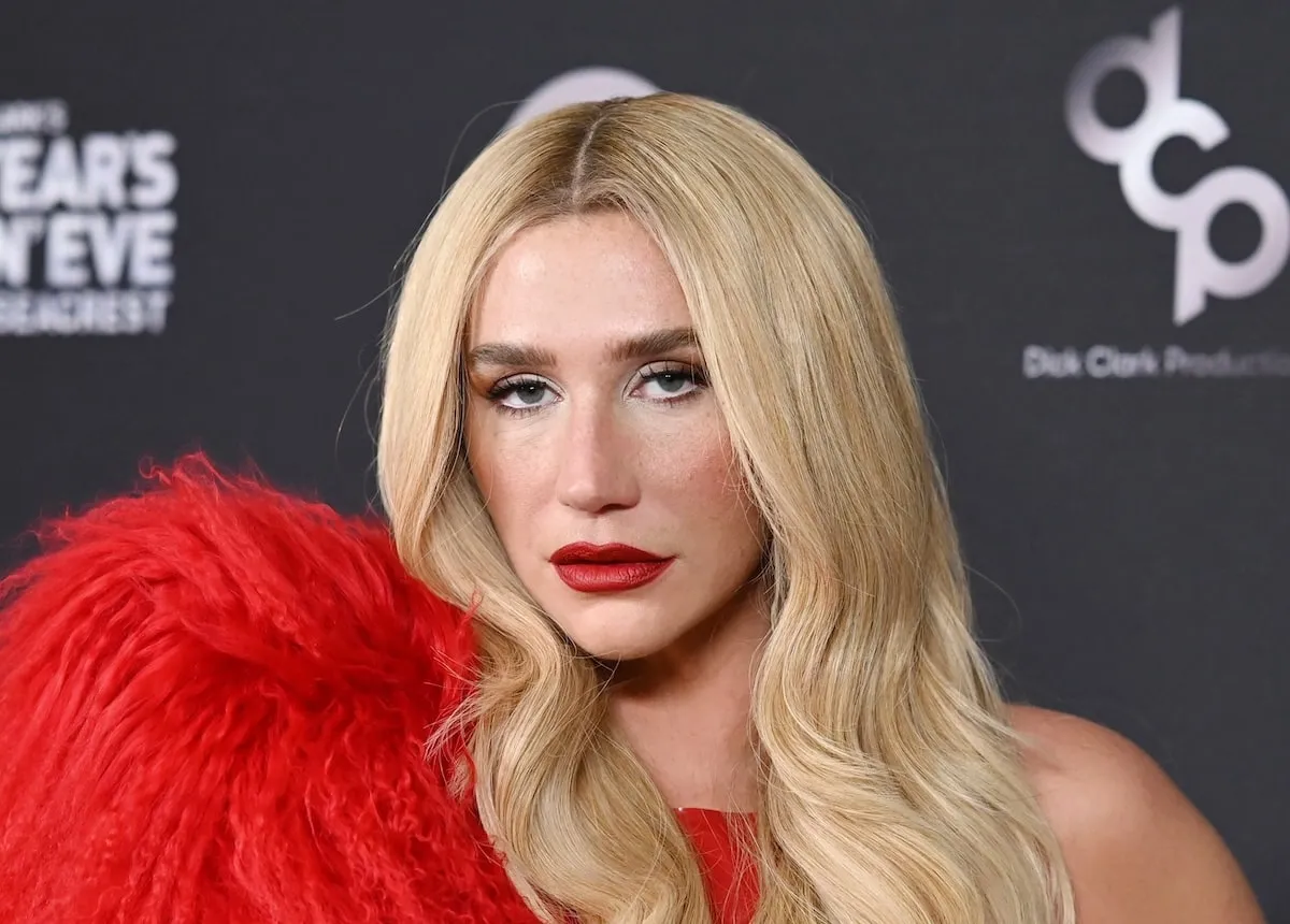 Wearing a red latex bodysuit and large red feather boa, Kesha stands on the red carpet and poses for photos before Dick Clark's New Year's Rockin' Eve with Ryan Seacrest on December 31, 2024