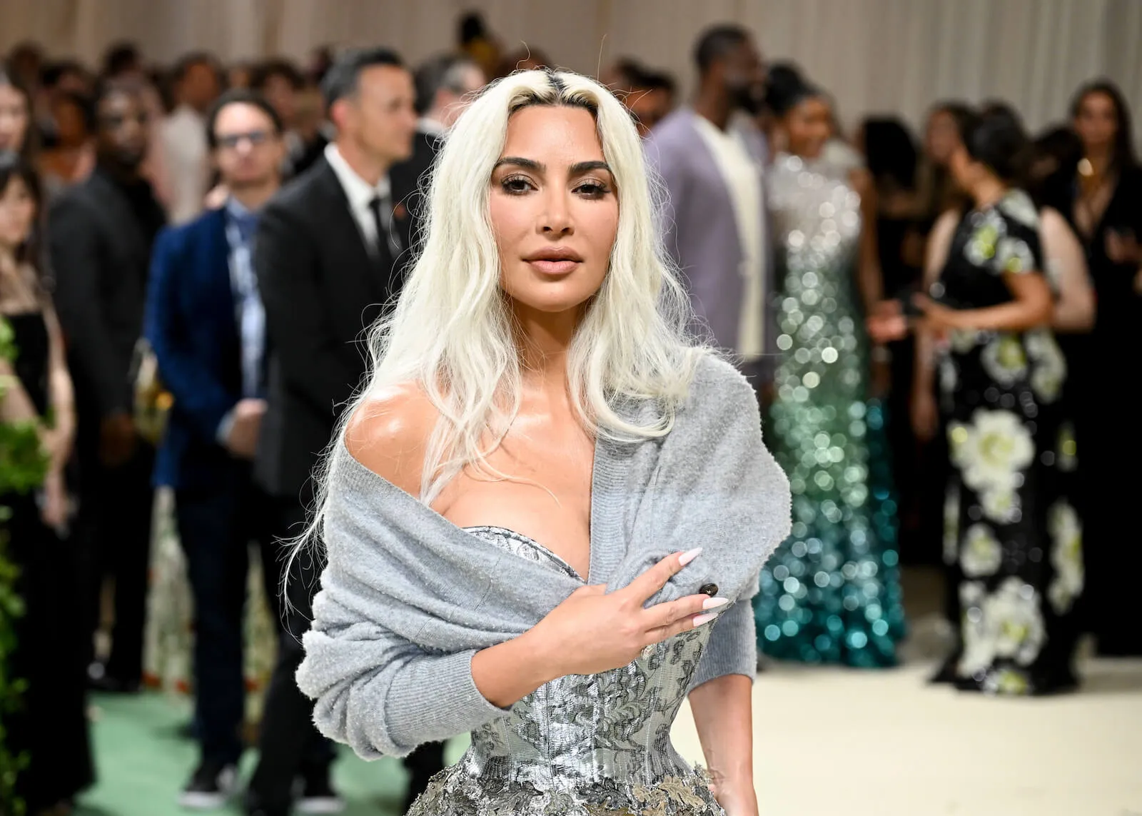 Kim Kardashian at the Met Gala in 2024. She bleached her hair and is wearing a shiny silver dress with a silver shawl draped over one shoulder.