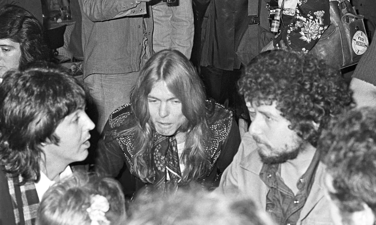 A black and white picture of Paul McCartney, Gregg Allman, and Bob Dylan talking together in a crowd.