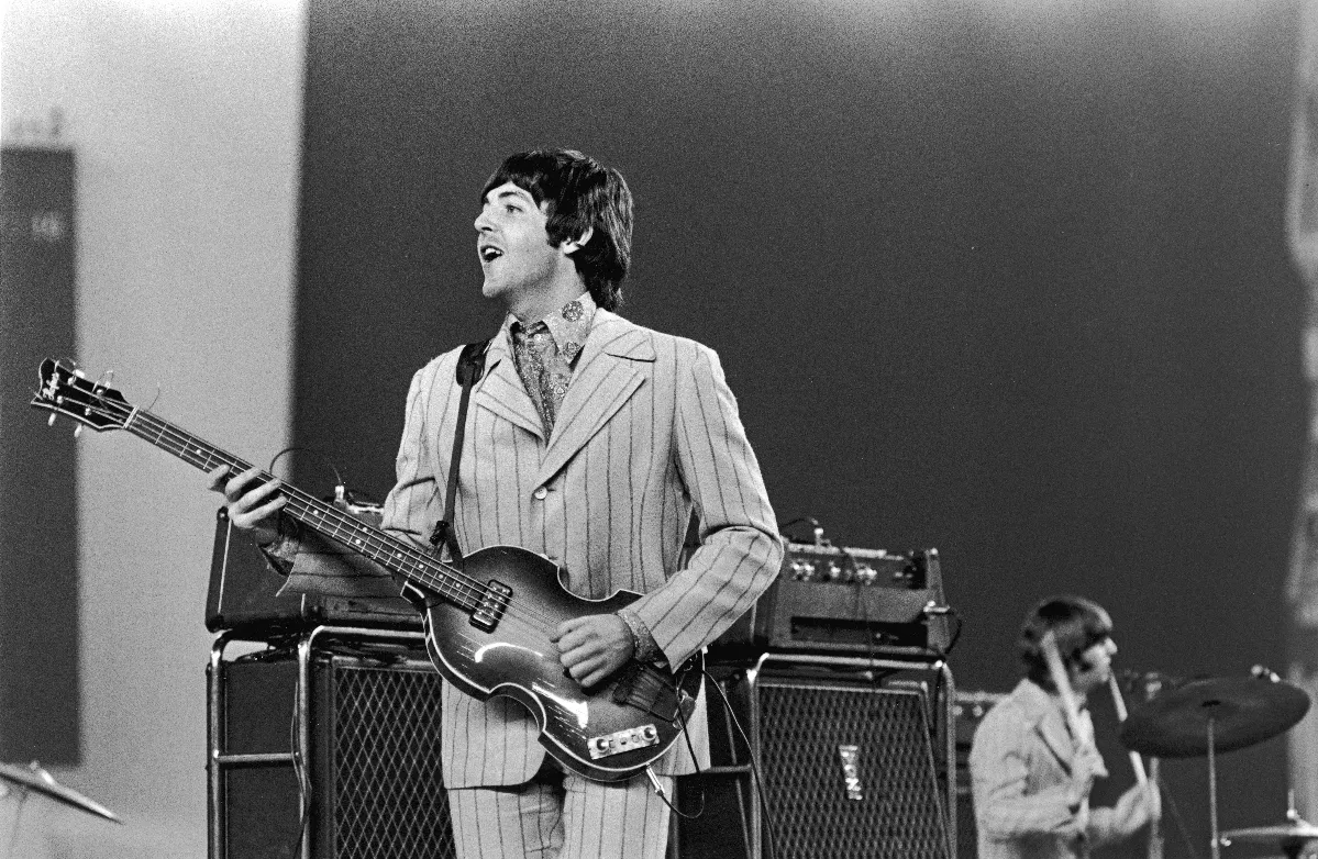 A black and white picture of Paul McCartney playing a bass guitar.