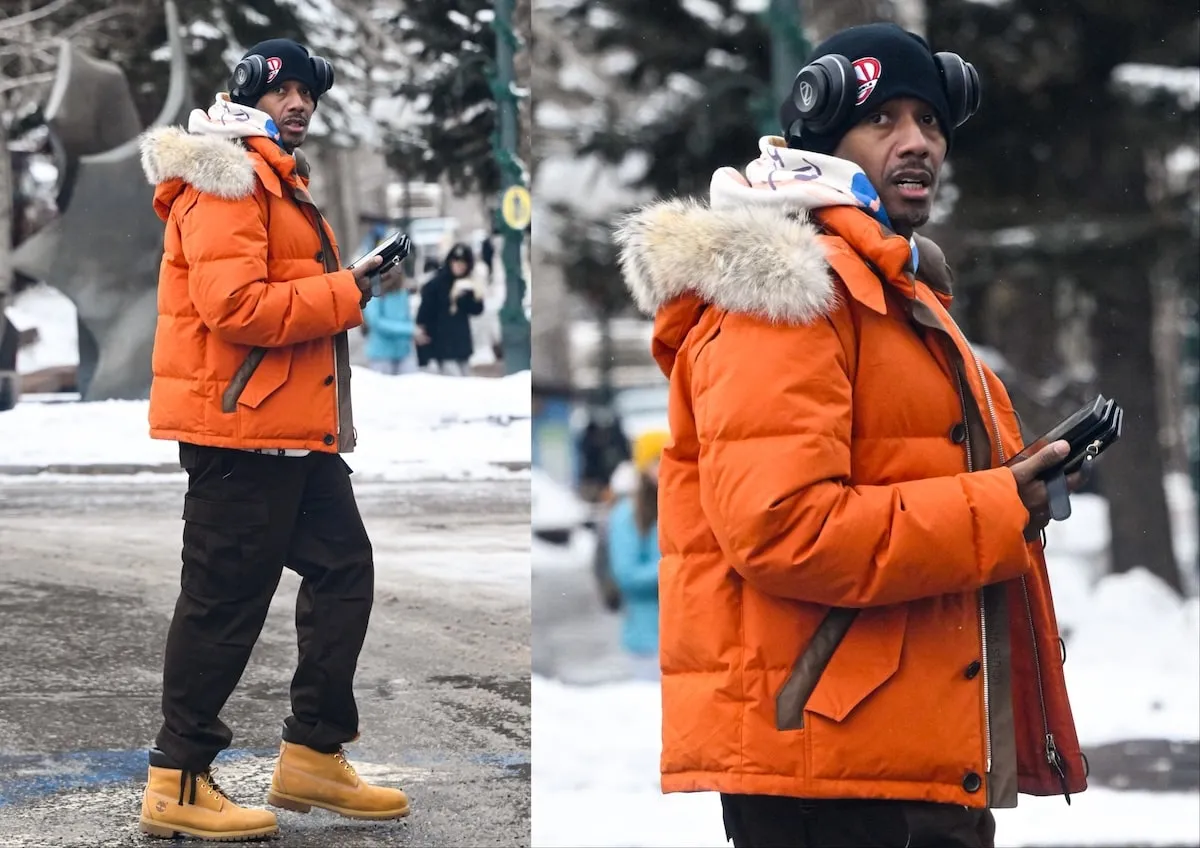 Wearing an orange jacket and black snow pants, Nick Cannon walks on an icy sidewalk in Aspen on December 26, 2024