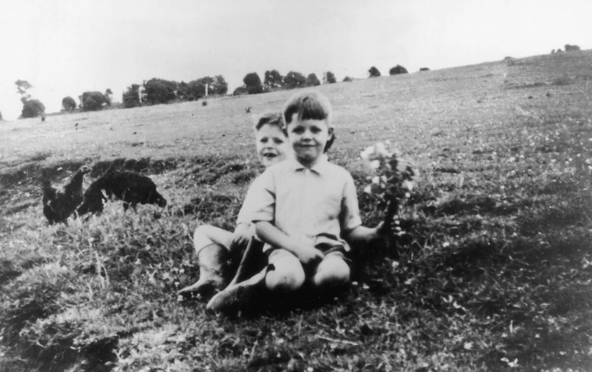 A black and white picture of Paul McCartney and his brother sitting in a field.