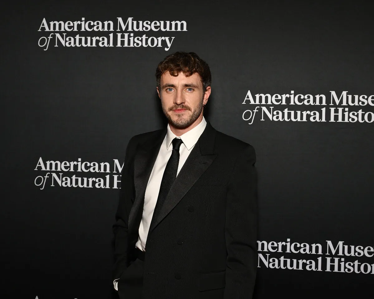 Paul Mescal wears a suit and stands in front of signs for the American Museum of Natural History.