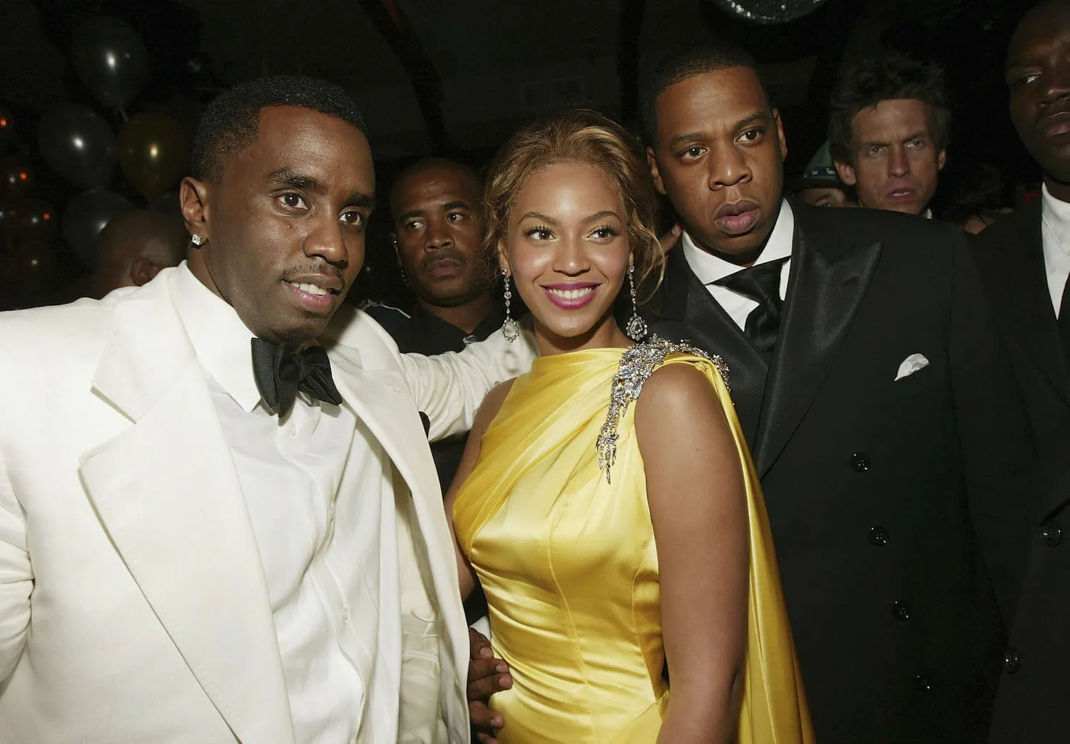 Sean 'Diddy' Combs, Beyoncé, and Jay-Z looking at a camera and posing in a dimly-lit afterparty in 2004