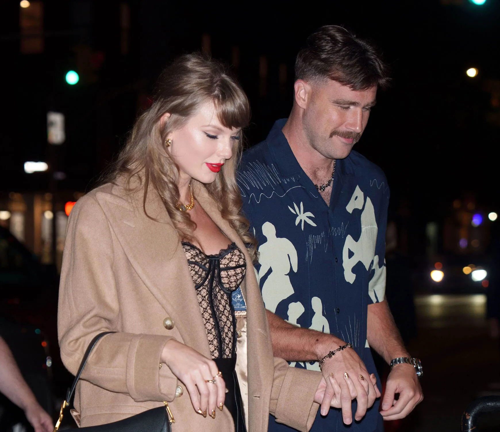 Taylor Swift and Travis Kelce walking hand in hand and looking down at night in New York City