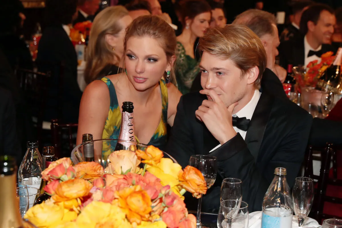 Taylor Swift and Joe Alwyn sit next to each other.