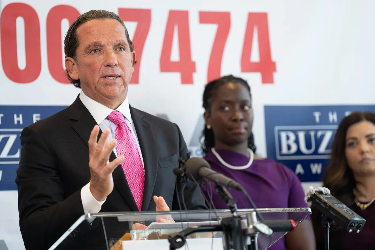 Tony Buzbee stands at a podium and speaks. Two women stand behind him.