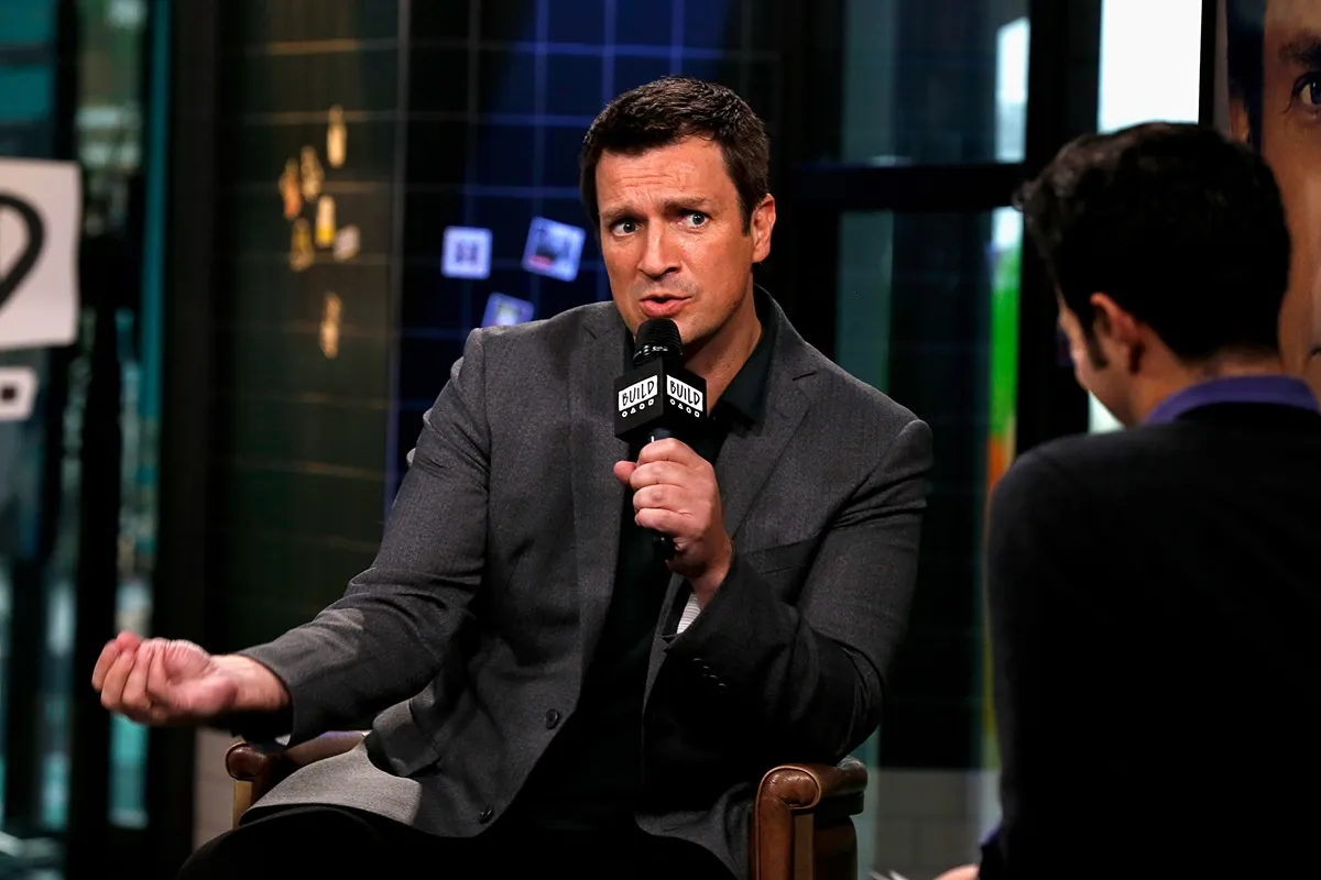 Nathan Fillion sitting down holding a microphone while attending AOL'S 'BUILD' series.