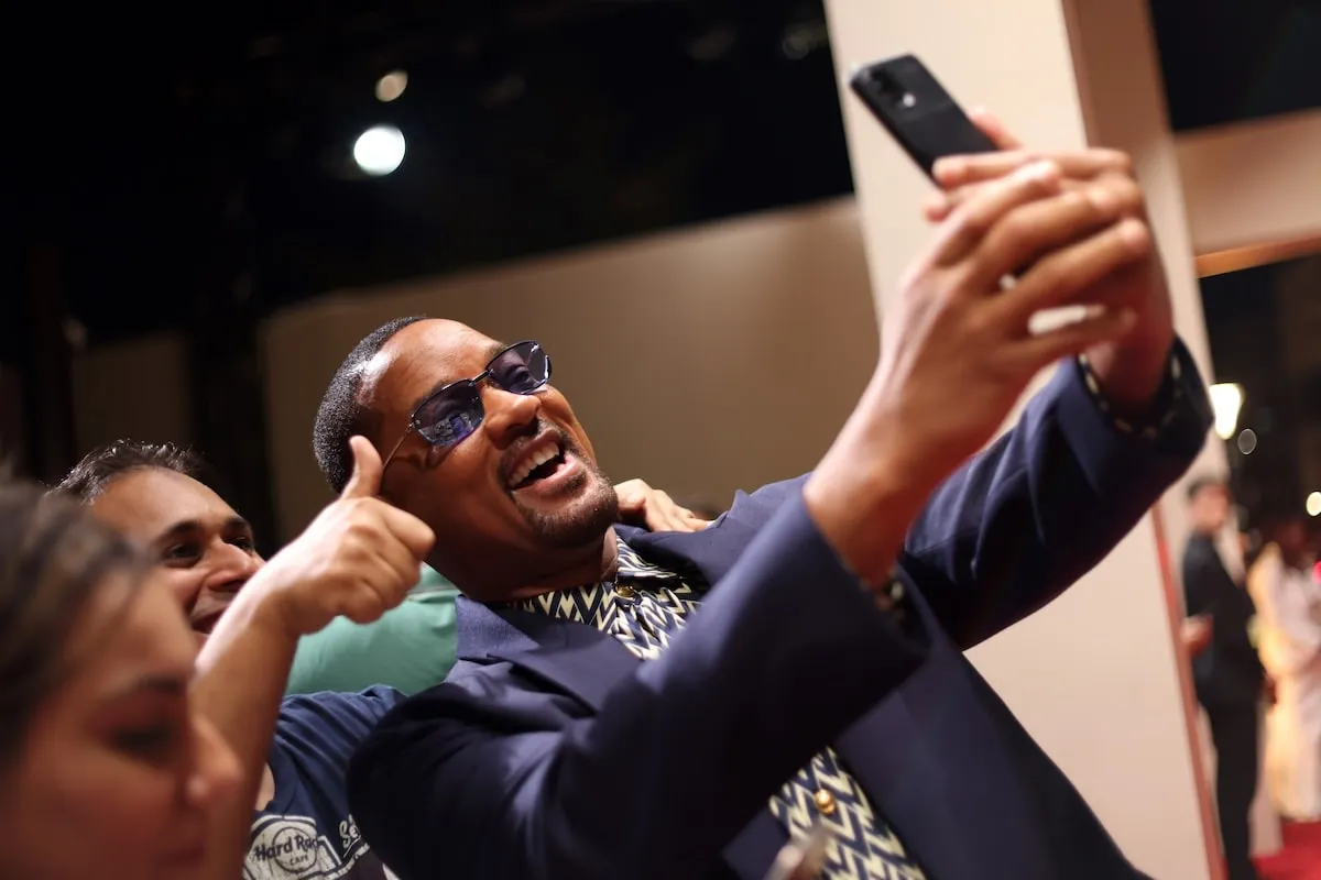 Wearing a navy suit, Will Smith takes a selfie with a fan at the Opening Ceremony at the Red Sea International Film Festival 2024