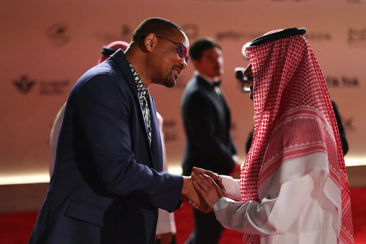 Wearing a navy suit, Will Smith greets and shakes the hand of a supporter at the Red Sea International Film Festival 2024