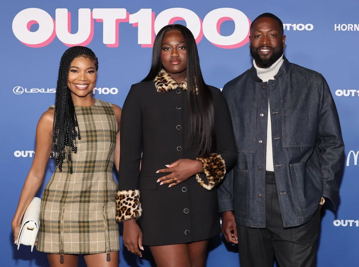 Wearing a black dress with leopard print cuffs, Zaya Wade smiles with her parents at the Out100 Gala