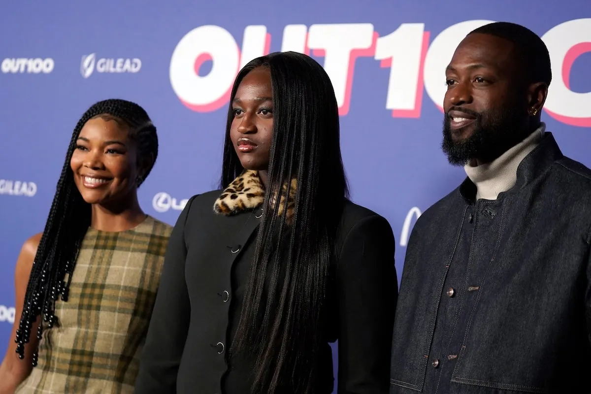 Wearing a black dress with leopard print cuffs, Zaya Wade smiles with her parents at the Out100 Gala