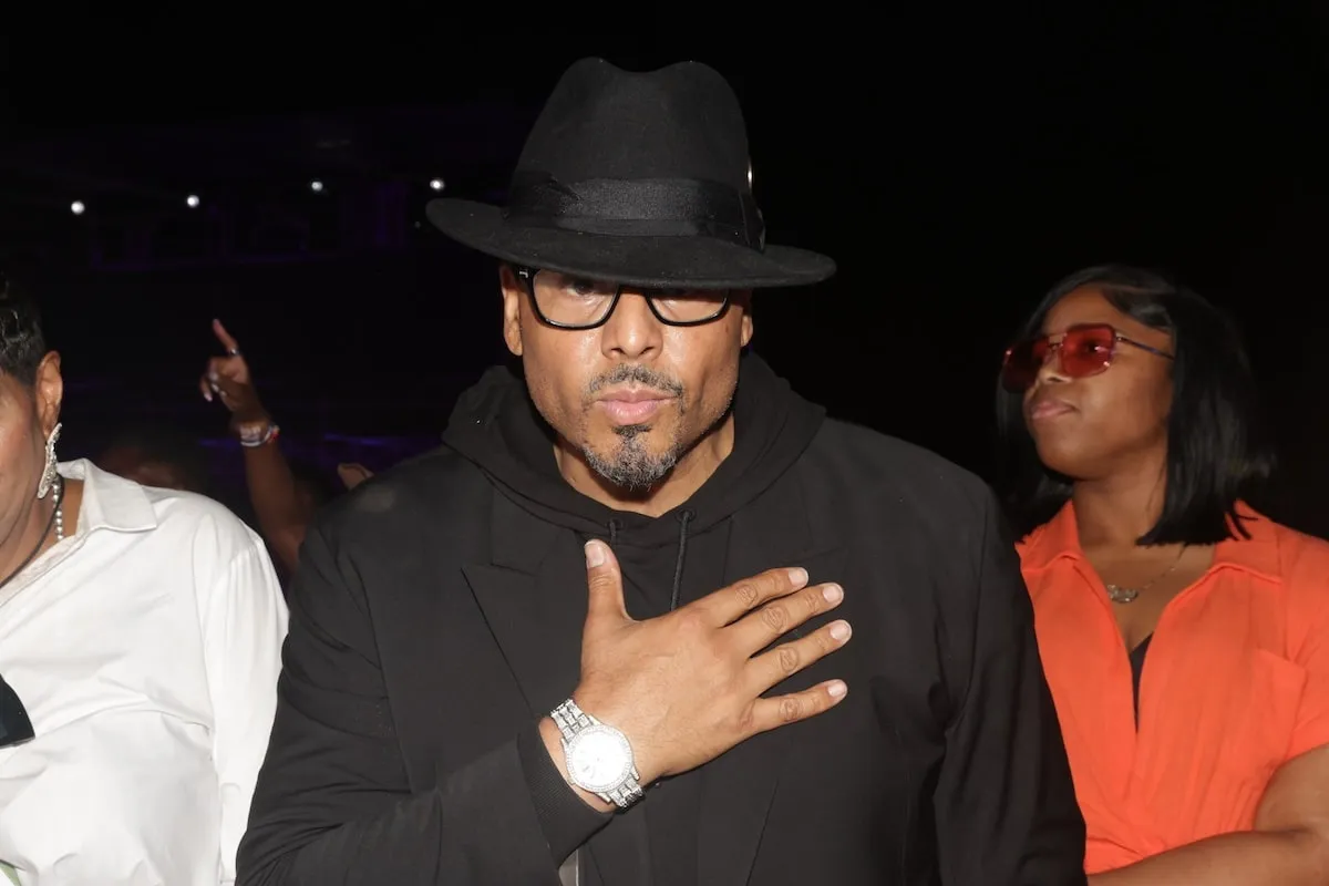 Wearing a black hoodie and hat, Al B. Sure holds his hand to heart for the camera