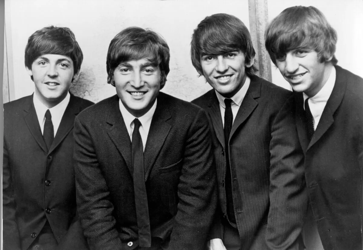 A black and white picture of The Beatles wearing suits and standing in a row.