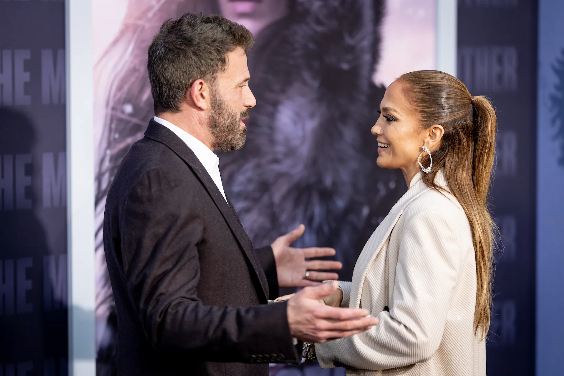 Ben Affleck and Jennifer Lopez looking at each other and about to embrace in a hug at a movie premiere. Affleck is wearing a suit jacket and Lopez is wearing a cream blazer.