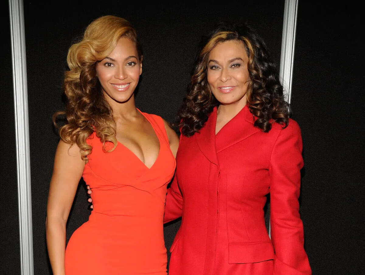 Beyonce and her mother, Tina Knowles, wear orange and stand with their arms around each other.