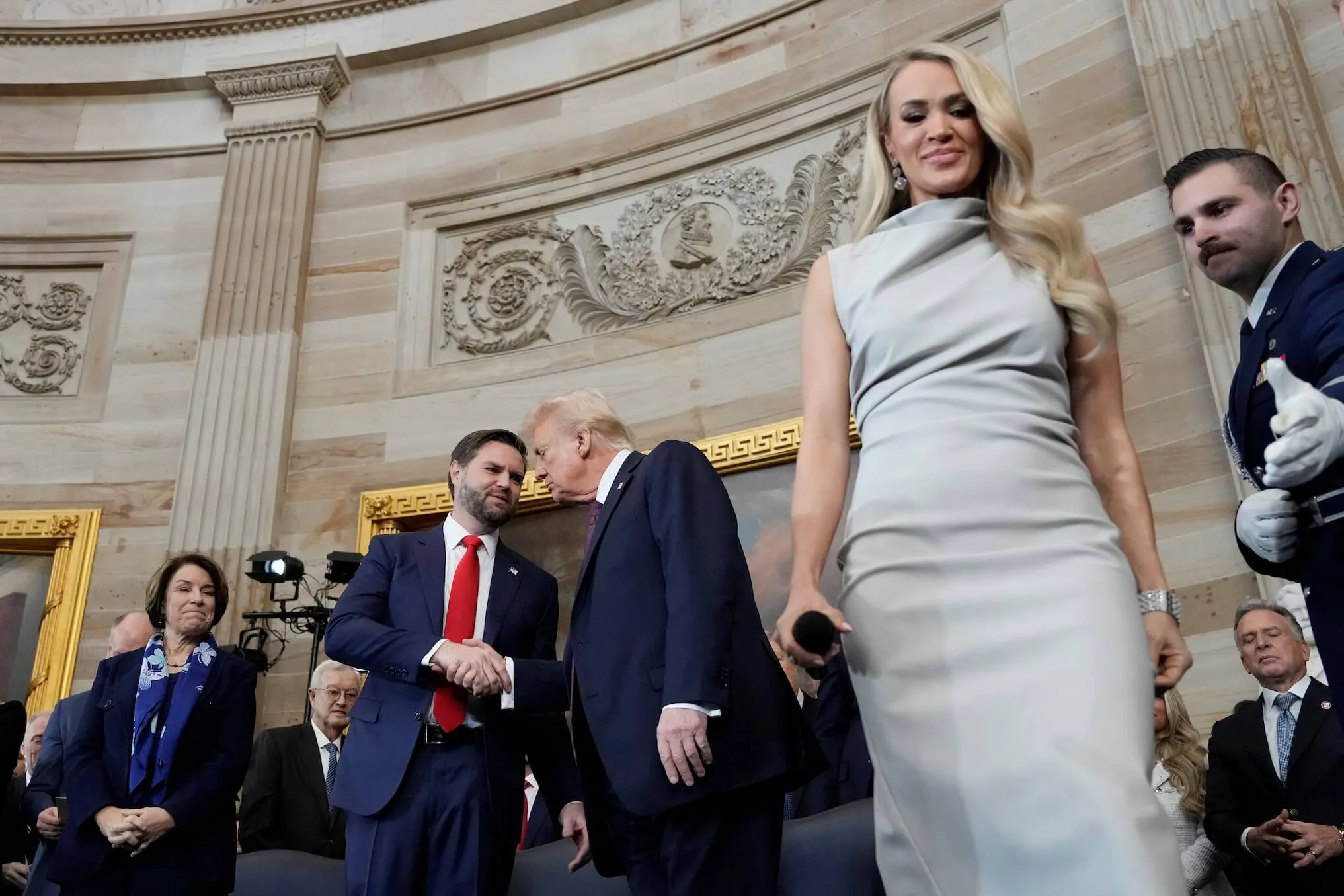 Carrie Underwood in a gray dress walking past JD Vance and Donald Trump at the inauguration