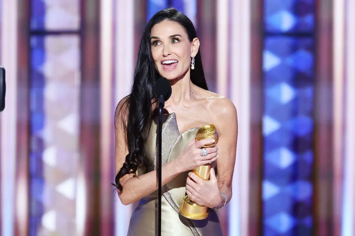 Demi Moore holds a Golden Globe award and speaks into a microphone.