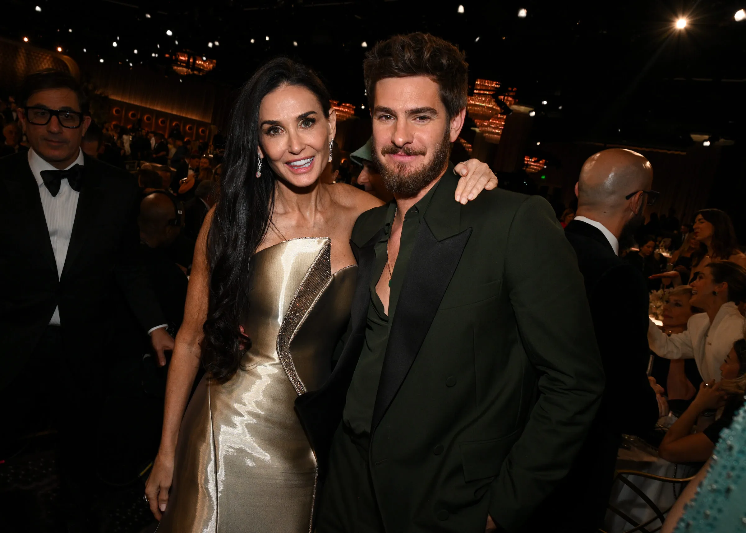 Demi Moore with her arm around Andrew Garfield's shoulder smiling at the camera during the 82nd Annual Golden Globes 