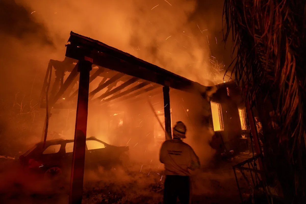 A firefighter stands in front of a burning home in Altadena