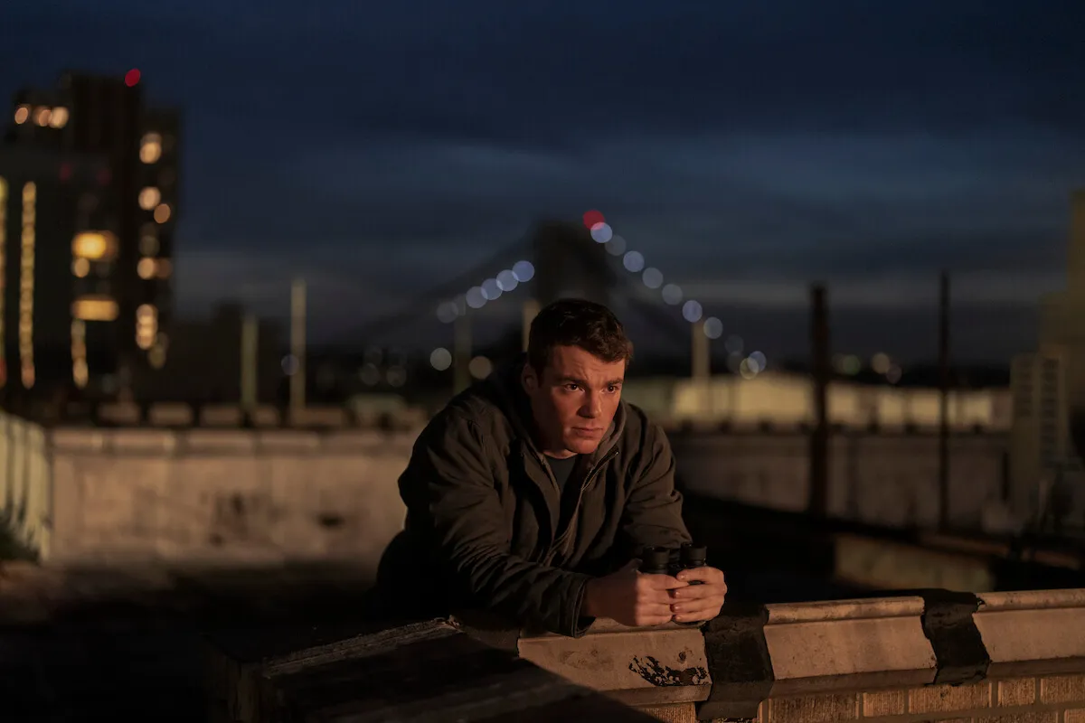 Gabriel Basso leans against a wall and looks on in Netflix's 'The Night Agent' Season 2