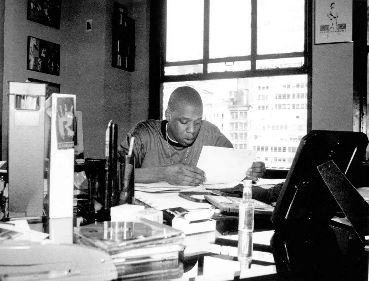 A black and white picture of Jay-Z sitting at a desk and reading from a paper.