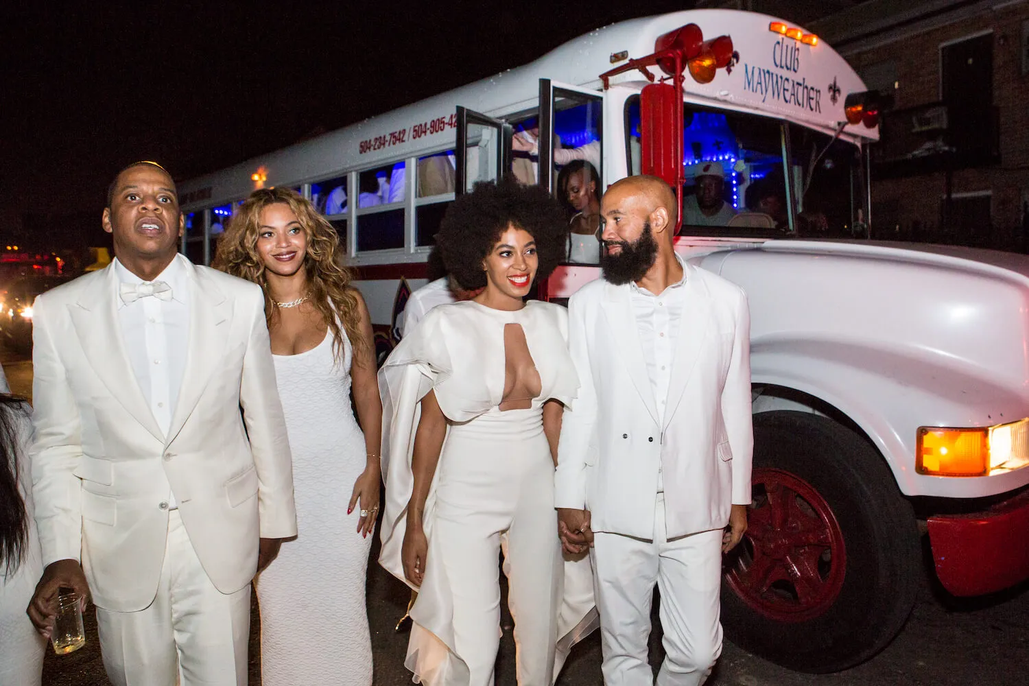 Jay-Z, Beyoncé Knowles, Solange Knowles, and Alan Ferguson walking together at night. They are all wearing white and next to a white school bus.