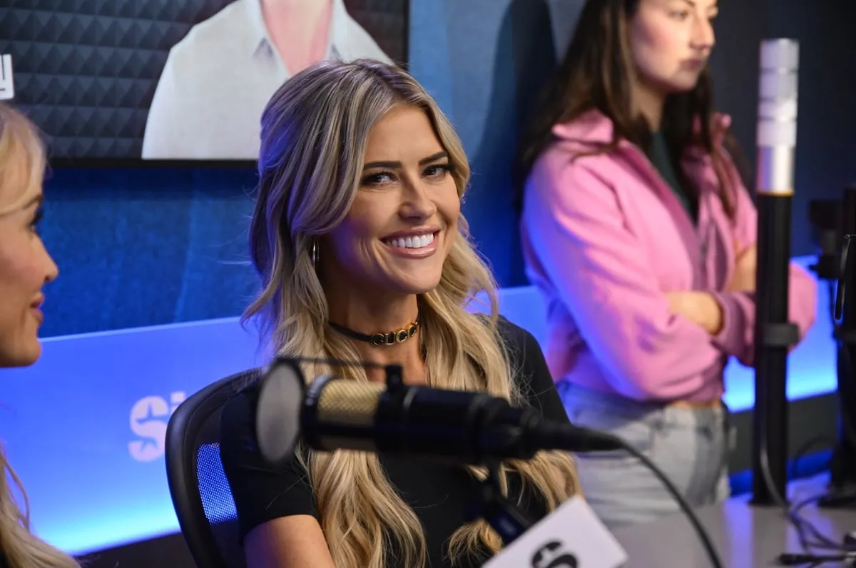 Wearing a black tee shirt and choker, Christina Haack smiles while recording the Jeff Lewis Live radio show