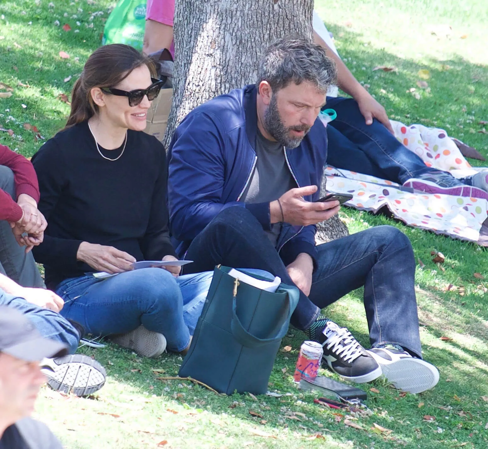 Jennifer Garner and Ben Affleck sitting next to each other on grass in Los Angeles. Affleck is looking at his phone.