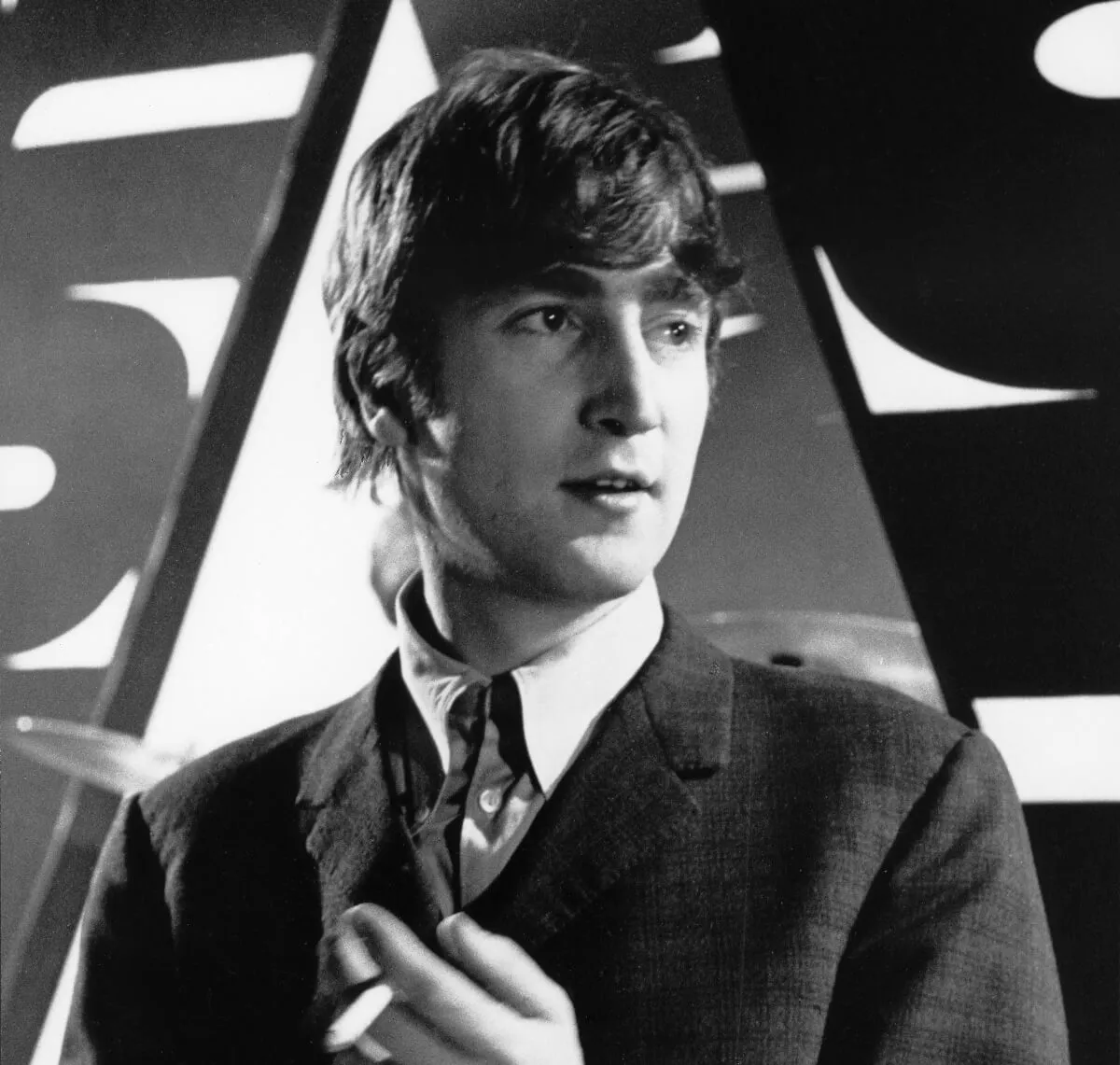 John Lennon wears a suit and holds a cigarette between his fingers.