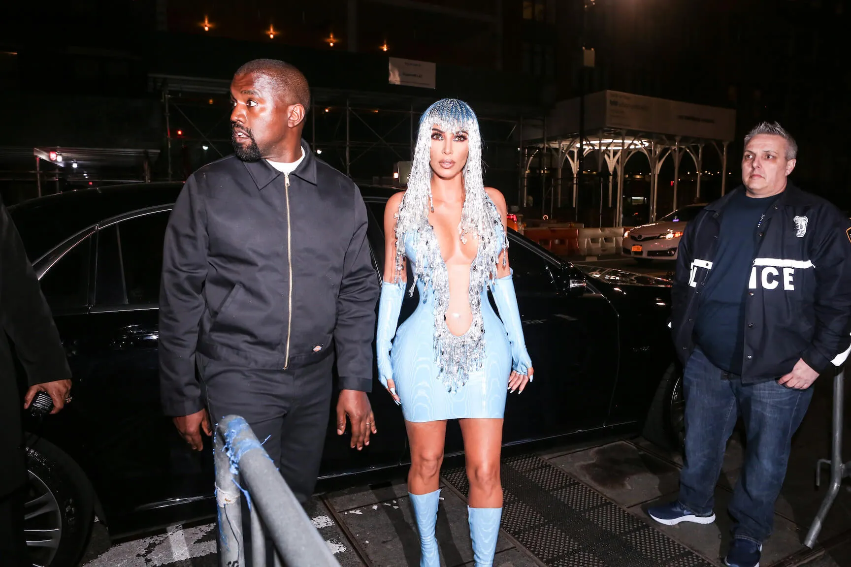 Kanye West walking next to Kim Kardashian, who's in a blue minidress and matching hair, at night