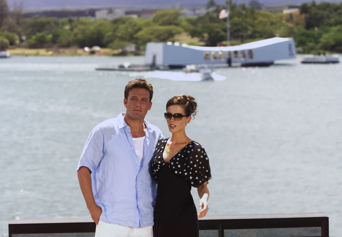 Kate Beckinsale wearing a black dress posing alongside Ben Affleck in a light blue shirt at the flight deck of the aircraft carrier USS John C. Stennis.