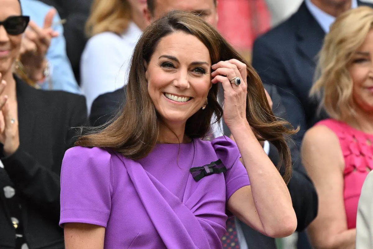 Kate Middleton, who is a future queen, tucks hair behind her ear and smiles.