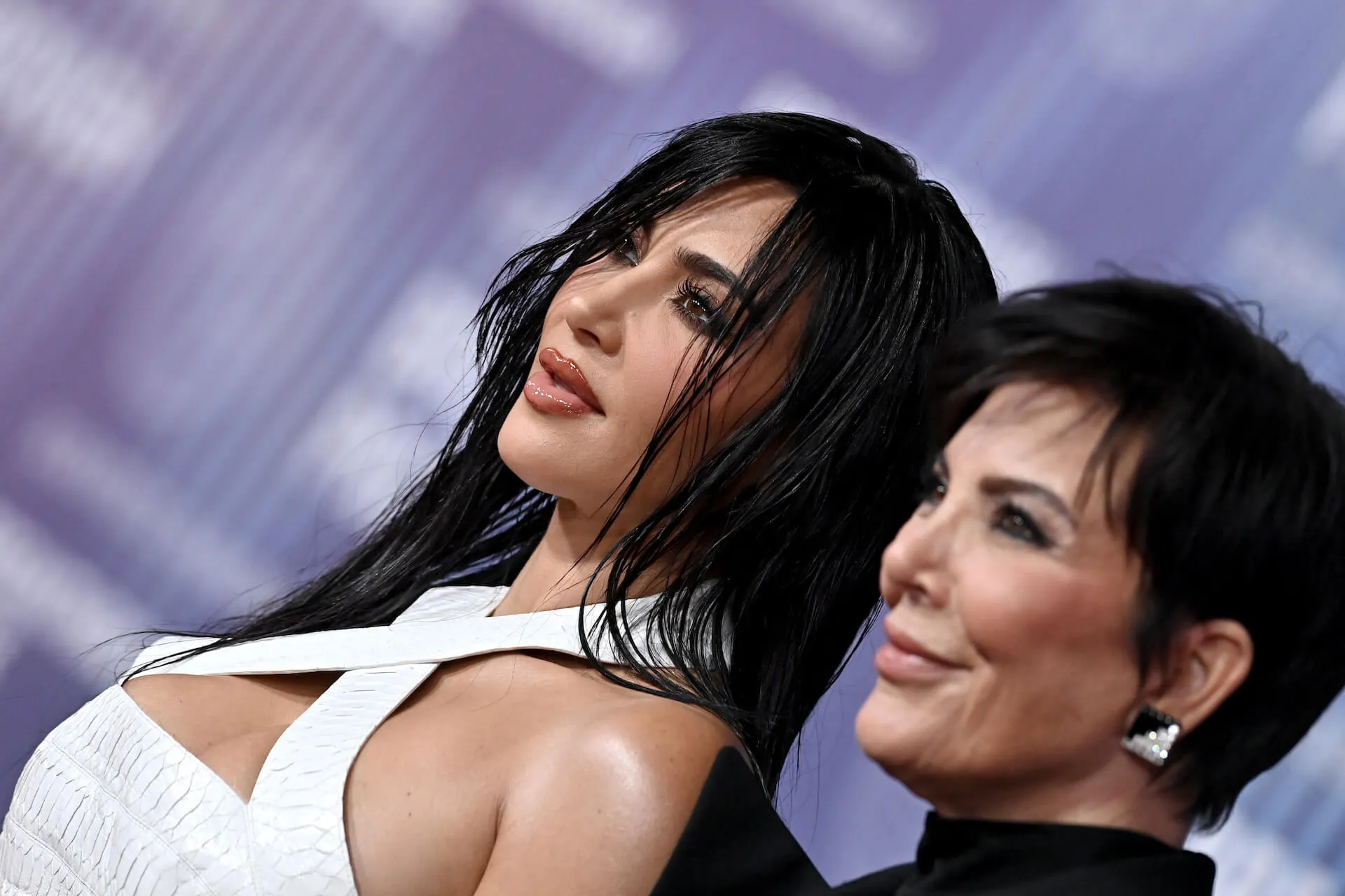 A close-up of Kim Kardashian's face angled by the photographer with Kris Jenner to her left. They're both looking forward and smiling slightly.