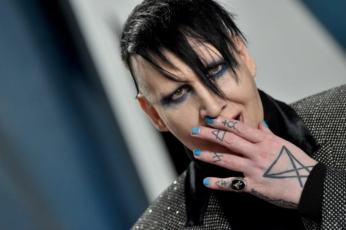 Marilyn Manson with spiky bangs and his hand against his mouth