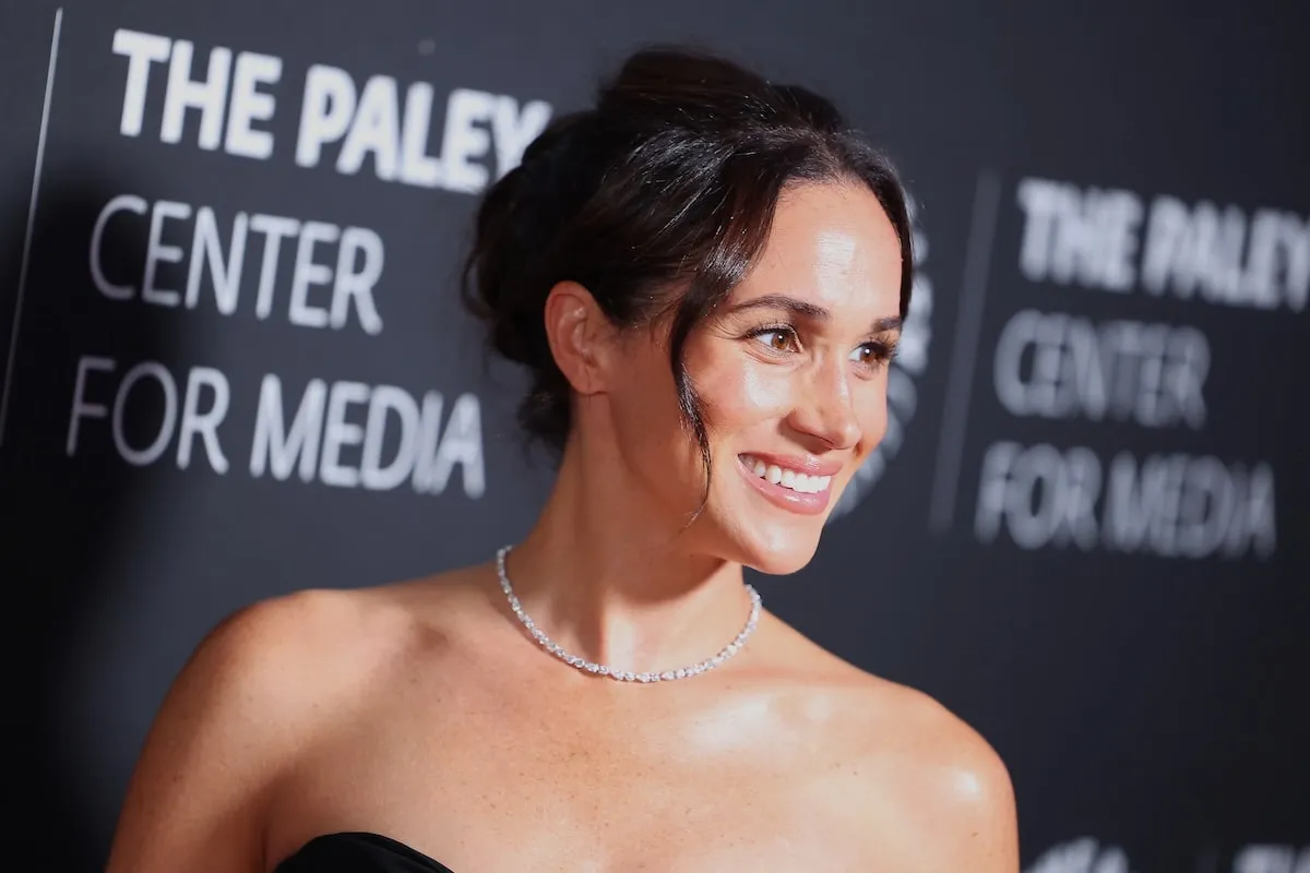 Wearing a diamond necklace, Meghan Markle smiles for cameras at a 2024 media event