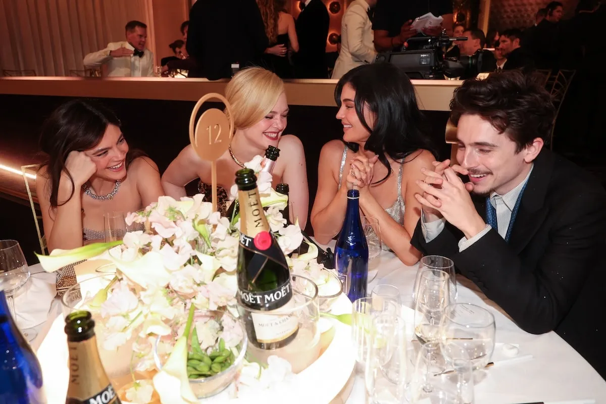 Celebrities Monica Barbaro, Elle Fanning, Kylie Jenner, and Timothée Chalamet laugh while sitting together at their table at the 2025 Golden Globes