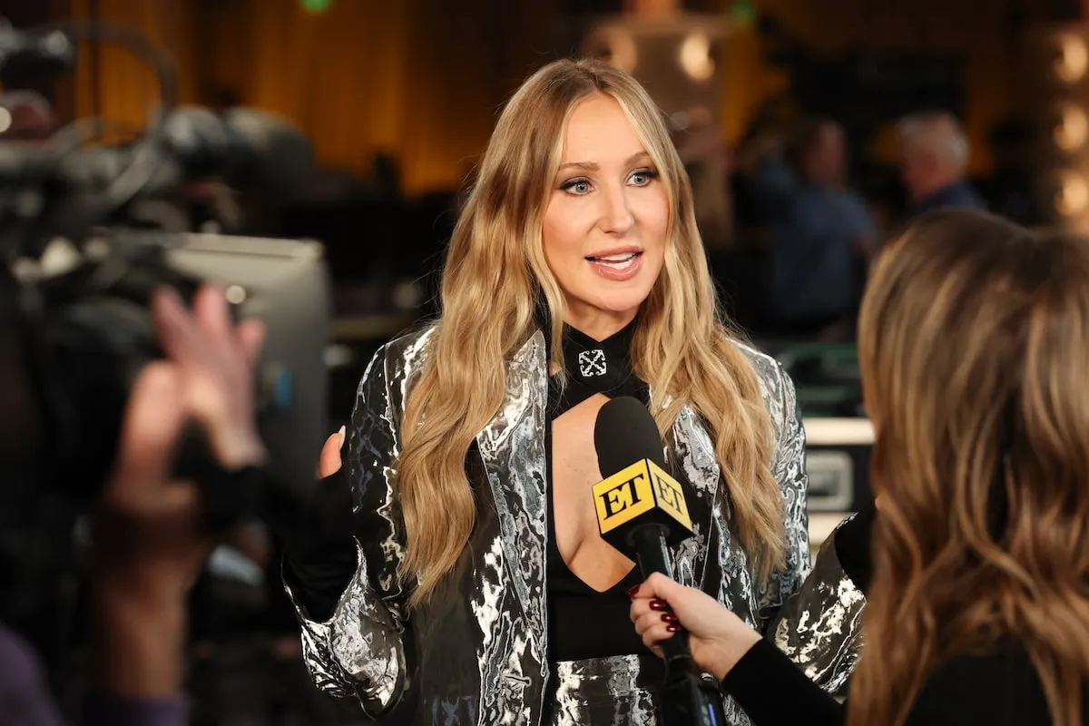 Wearing a black top and silver pants, Nikki Glaser speaks to reporters at the Red Carpet Rollout for the 82nd Annual Golden Globe Awards