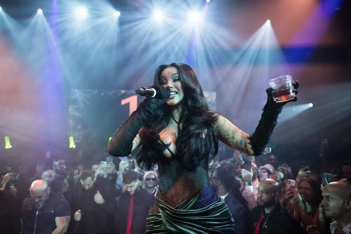 Wearing a black and green lace corset dress, Cardi B performs at Miami's E11EVEN nightclub while sipping Hennessy